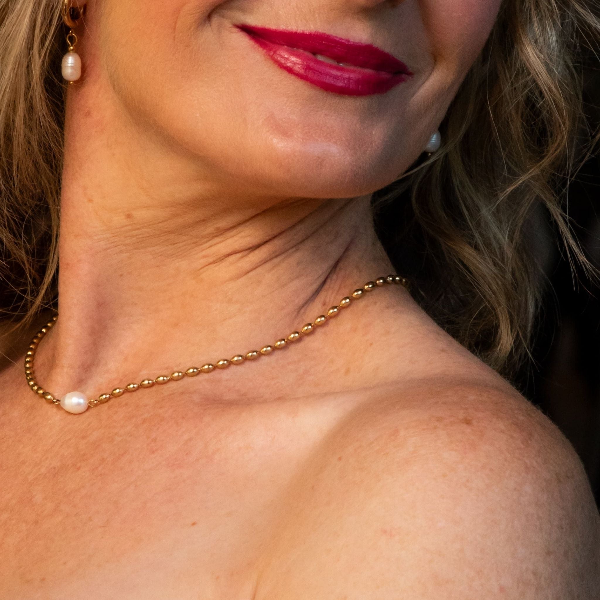 Close-up of a woman wearing a gold necklace with a pearl pendant.