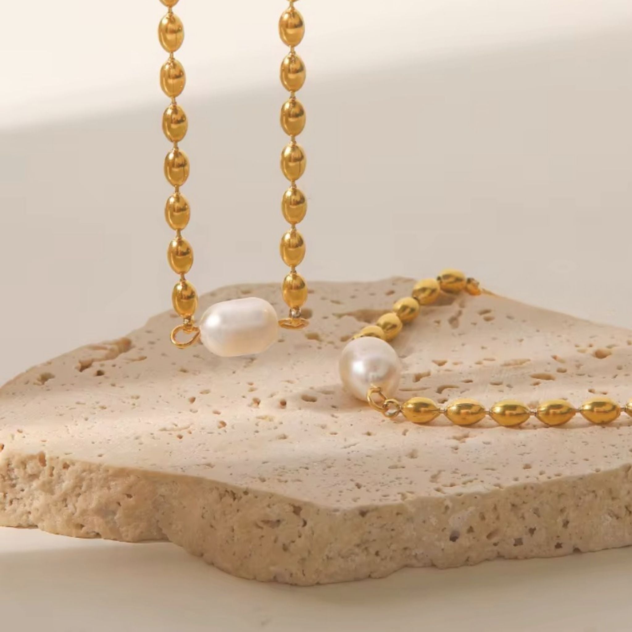 Gold beaded necklace with pearls on a textured stone surface