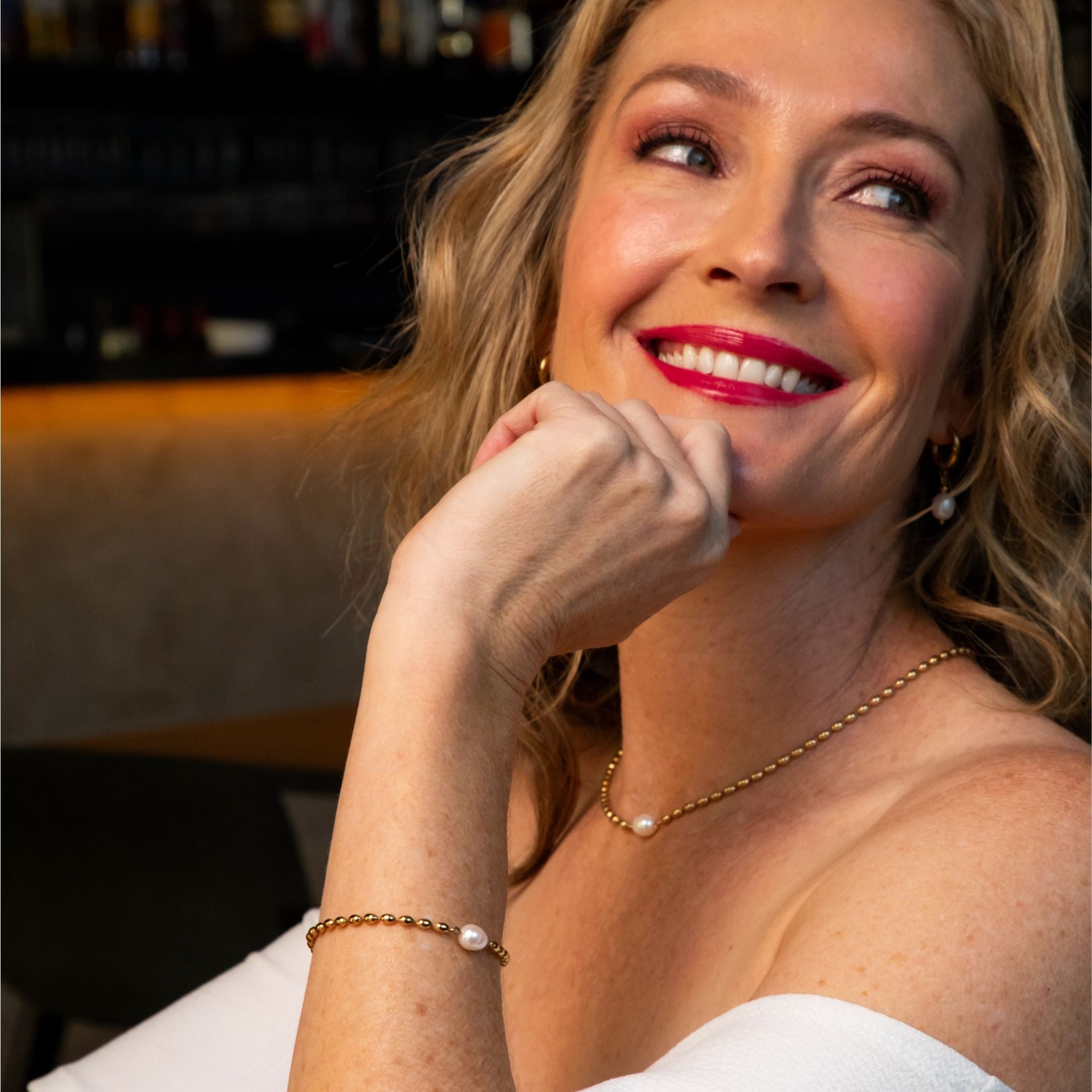 Woman with red lipstick and a gold necklace in a blurred indoor setting