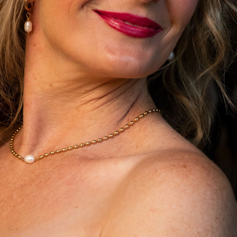 Close-up of a woman wearing a gold necklace with a pearl pendant.